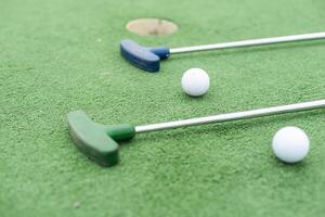 Mini-golf clubs and balls of different colors laid on artificial grass photo