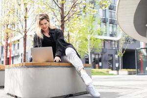 girl with a laptop on a bench in the park on a background of greenery photo