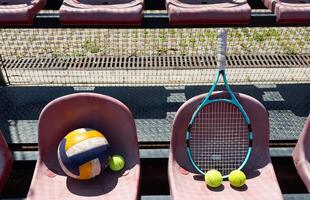 a tennis racket, balls and a volleyball on a bench on the sports tribune photo