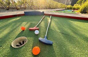 Assorted miniature golf putters and balls askew on synthetic grass. photo