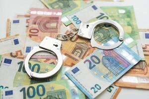 Pair of metal police handcuffs on Euros banknotes money cash background. Corruption, dirty money, gambling or financial crime ideas concept. photo