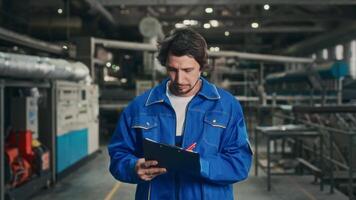 een mannetje ingenieur in een blauw uniform wandelingen door de fabriek werkplaats en cheques de in werking parameters van een automatisch productie lijn. werk Aan instelling omhoog automatisch apparatuur. video