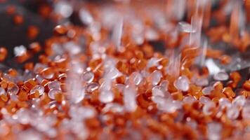 Macro frame of white and orange plastic granules. The polymer composite is poured into a tank for further production and casting in special molds. Production video