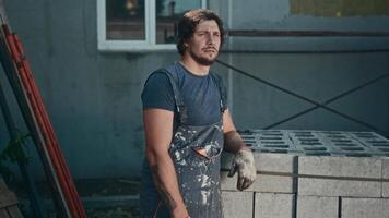 Portrait of a handyman at a construction site. A man in worn, dirty overalls is engaged in hard and low-skilled labor. video