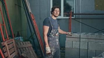 Portrait of a handyman at a construction site. A man in worn, dirty overalls is engaged in hard and low-skilled labor. video