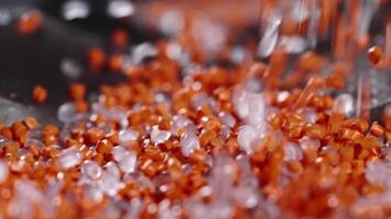 Macro frame of white and orange plastic granules. The polymer composite is poured into a tank for further production and casting in special molds. Production video