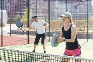 Portrait of positive young woman and adult man standing on padel tennis court, holding racket and ball, smiling photo