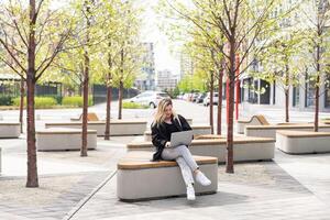 Young beautiful business woman sitting on a bench in the sunny city photo