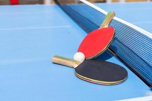 Two table tennis or ping pong rackets and ball on blue table with net photo