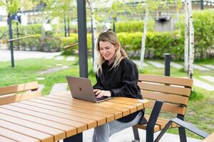 girl with a laptop on a bench in the park on a background of greenery photo