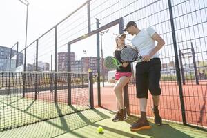 alegre atlético Pareja riendo durante padel tenis partido en al aire libre corte. foto