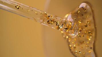 vloeistof gel of serum met gouden deeltjes stromen uit pipet. druppelaar met kunstmatig Product, verticaal formaat video