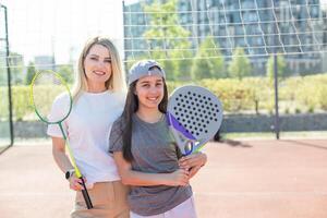 Happy caucasian mother and daughter playing padel tennis and badminton on tennis court outdoors photo