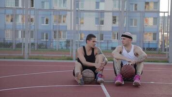 Two guys are sitting on the basketball court with balls and communicate. Spin the ball on his finger. video