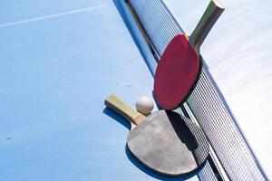 Two table tennis or ping pong rackets and ball on blue table with net photo