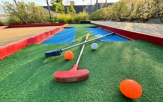 Mini-golf clubs and balls of different colors laid on artificial grass. photo