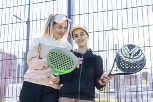 positive mother and daughter standing on court with padel rackets photo