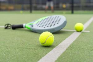 Yellow balls on grass turf near padel tennis racket behind net in green court outdoors with natural lighting. Paddle is a racquet game. Professional sport concept with copy space. photo