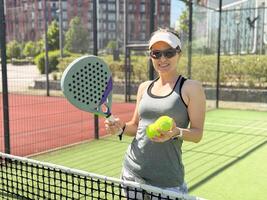 Portrait of active emotional woman playing padel tennis on open court in summer, swinging racket to return ball over net .. photo