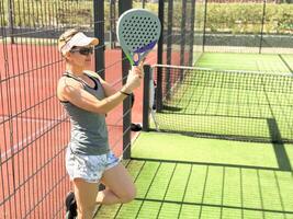 Portrait of active emotional woman playing padel tennis on open court in summer, swinging racket to return ball over net .. photo