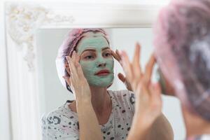 mujer utilizar un facial mascarilla. ella es mirando en el espejo. foto