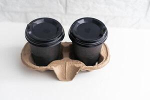 Takeaway paper coffee cups in cardboard holder on wooden table against black background, space for text. photo