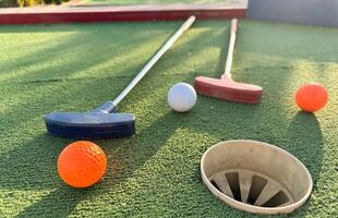 Mini-golf clubs and balls of different colors laid on artificial grass. photo