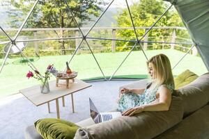 Young caucasian woman using and watching on laptop computer on in dome camping hotel. Tourism, vacation and weekend. photo