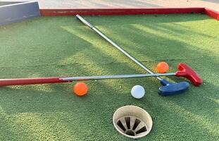 Mini-golf clubs and balls of different colors laid on artificial grass. photo