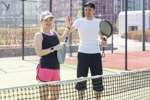 retrato de positivo joven mujer y adulto hombre en pie en padel tenis corte, participación raqueta y pelota, sonriente foto