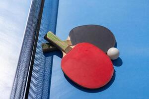 Two table tennis or ping pong rackets and ball on blue table with net photo