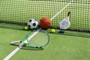 A variety of sports equipment including an american football, a soccer ball, a tennis racket, a tennis ball, and a basketball photo