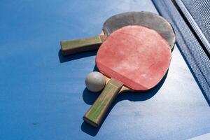 Two table tennis or ping pong rackets and ball on blue table with net photo