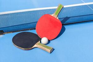 Two table tennis or ping pong rackets and ball on blue table with net photo