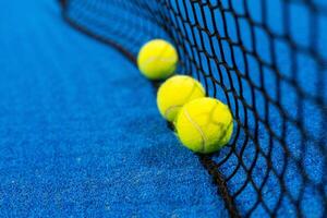 several balls by the net on a blue paddle tennis court photo