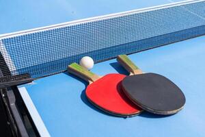 Red and black Table Tennis Paddles and ball on the blue table tennis table with net. Ping Pong concept with copy space photo