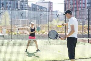 retrato de positivo joven mujer y adulto hombre en pie en padel tenis corte, participación raqueta y pelota, sonriente foto