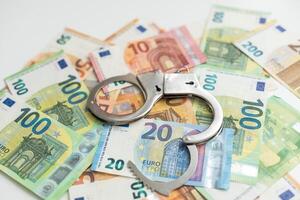 Police handcuffs lies on a set of green monetary denominations of 100 euros. A lot of money forms an infinite heap photo