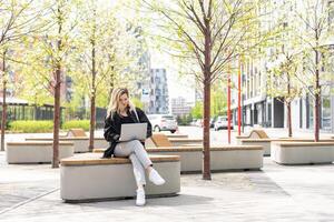 girl with a laptop on a bench in the park on a background of greenery photo