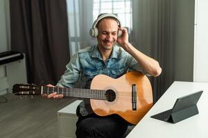 joven hombre sentado en su habitación y acecho guitarra tutorial en ordenador portátil foto