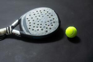 Detailed background of black and white padel racket and ball on black background. Top view. photo