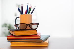 Stack of books with colored spines, colorful pencils in a cup photo