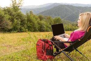 un mujer en un Deportes calentar traje trabajos en un ordenador portátil al aire libre en un montañoso área. foto