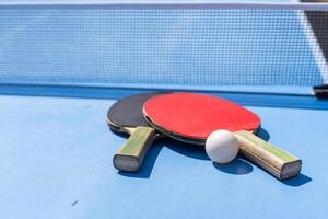 Two table tennis or ping pong rackets and ball on blue table with net photo