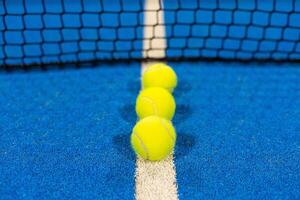 several balls by the net on a blue paddle tennis court photo