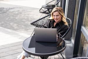 Businesswoman working with laptop in outdoor cafe. Corporate blog photo