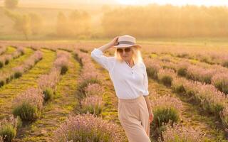 Young blond woman traveller wearing straw hat in lavender field surrounded with lavender flowers. photo