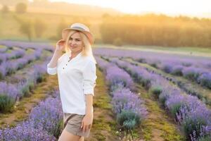 Young blond woman traveller wearing straw hat in lavender field surrounded with lavender flowers. photo