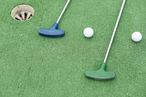 Mini-golf clubs and balls of different colors laid on artificial grass photo