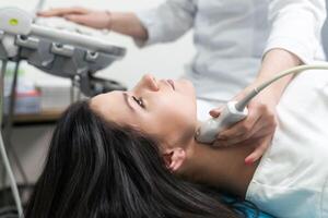 Doctor using ultrasound scanning machine for examining a thyroid of woman. photo